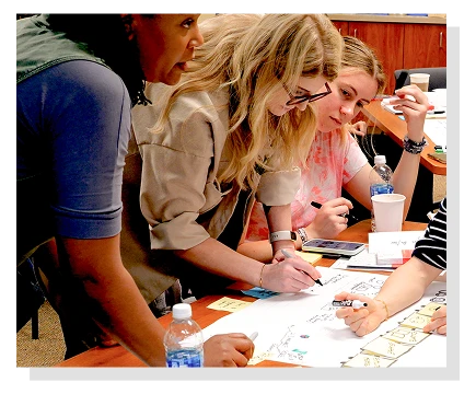 Photograph of several women collaborating on a work projects together with papers and writing utensils on a table.